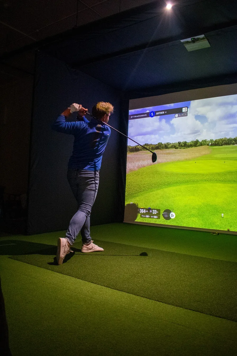 Golfer mid-swing in a Trackman simulator bay